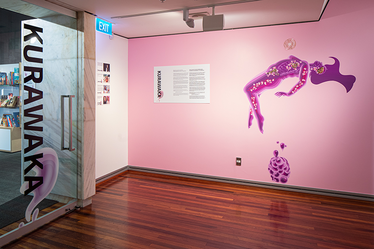 An exhibition room, words on the door are kurawaka. There is a pink wall with a silhouette of a pink transparent naked woman floating.