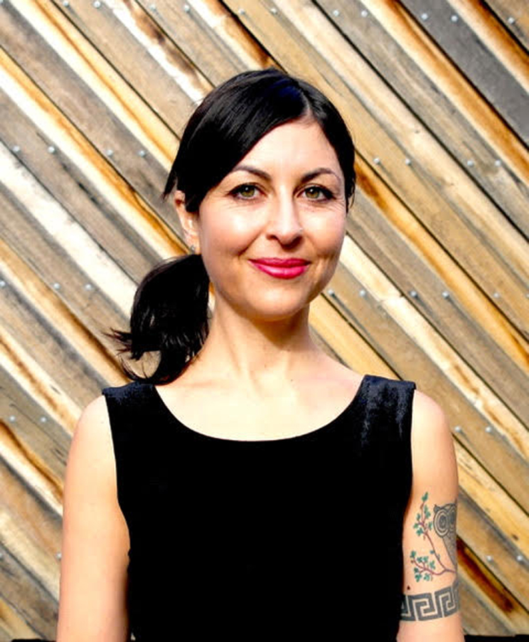 Woman wearing a black dress standing in front of a fence with diagonal palings.