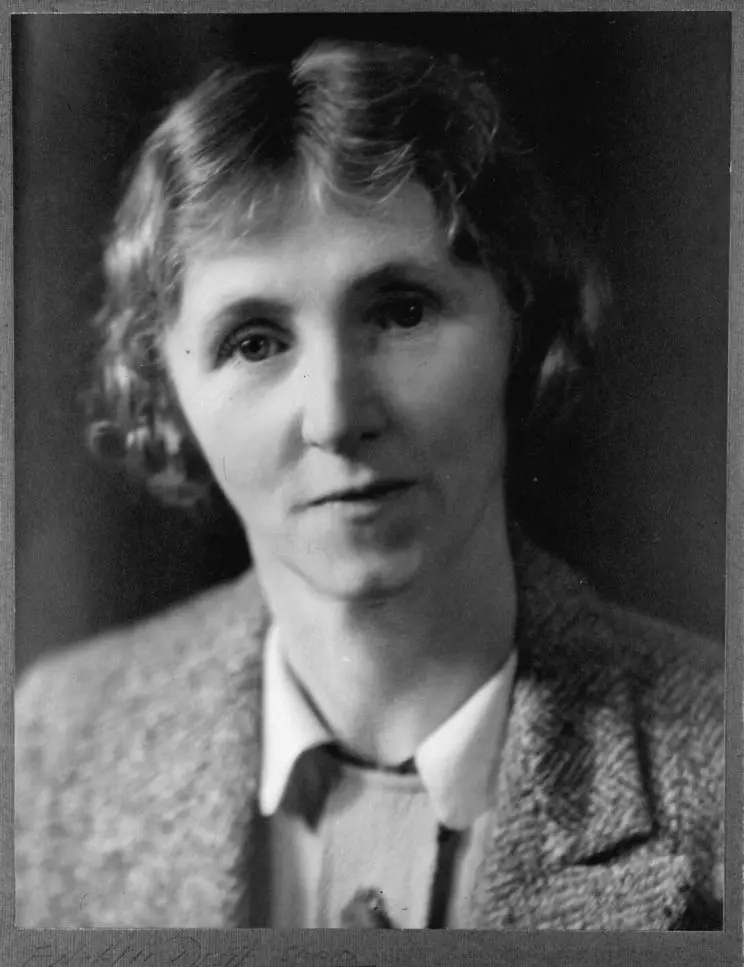 Black and white portrait photograph of a woman wearing a woolen jacket and white-collared shirt. 