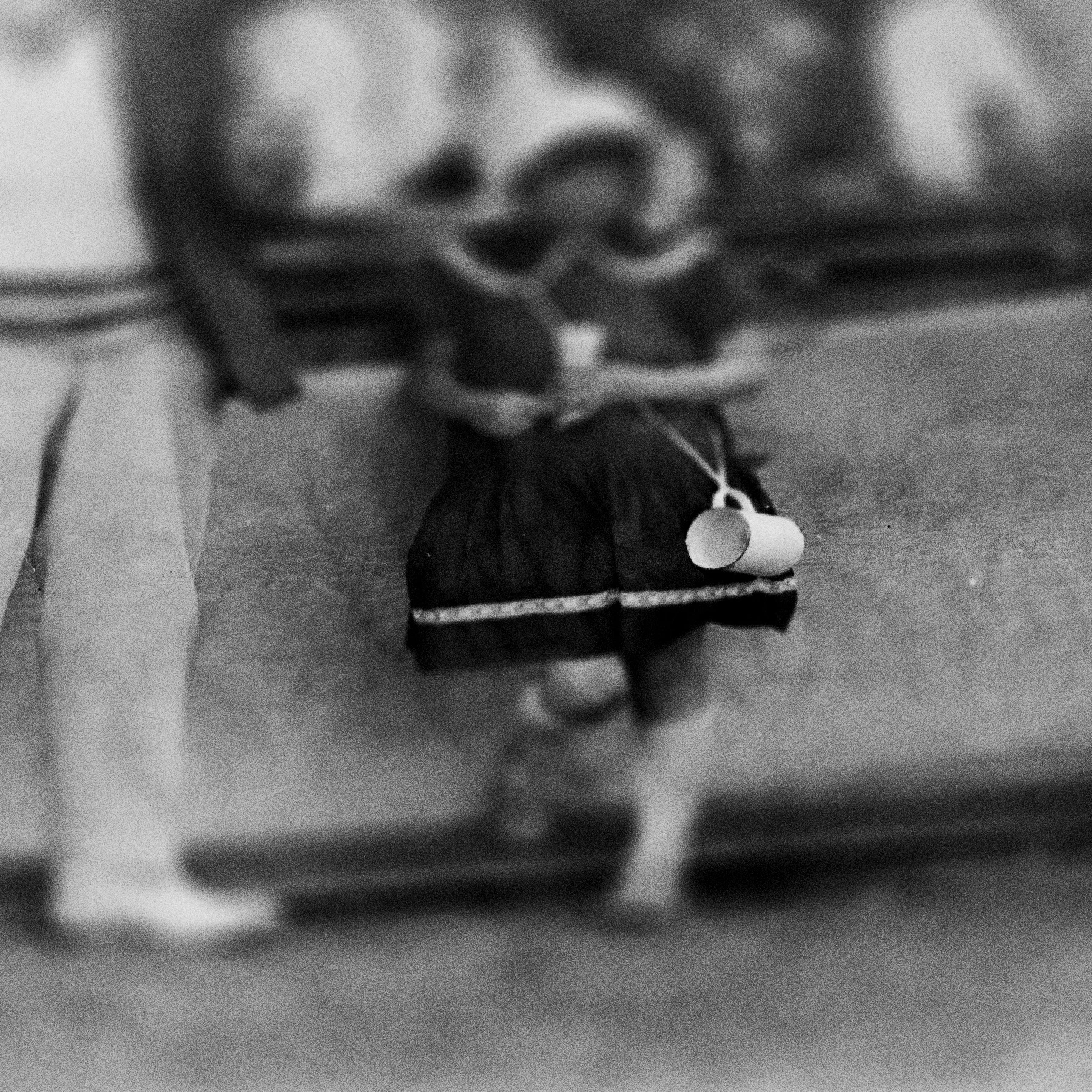 A young girl is seen leaning against a fence with an empty mug strung over her shoulder on a shoelace.