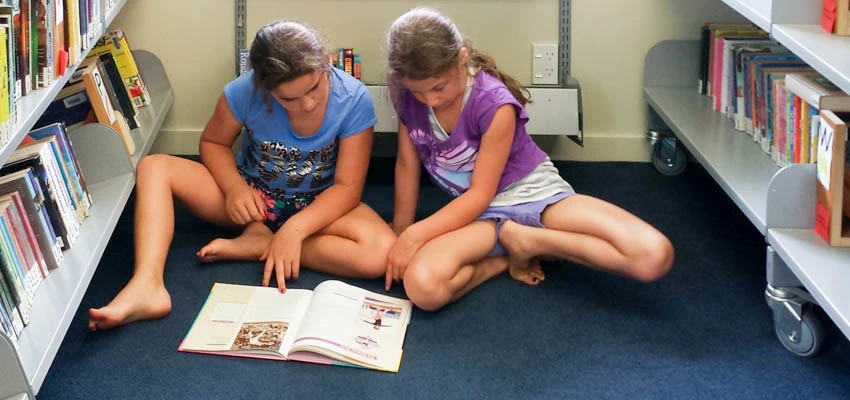 2 tweens reading a book in the school library