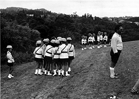 Black and white photo of two marching girl teams in a paddock. 