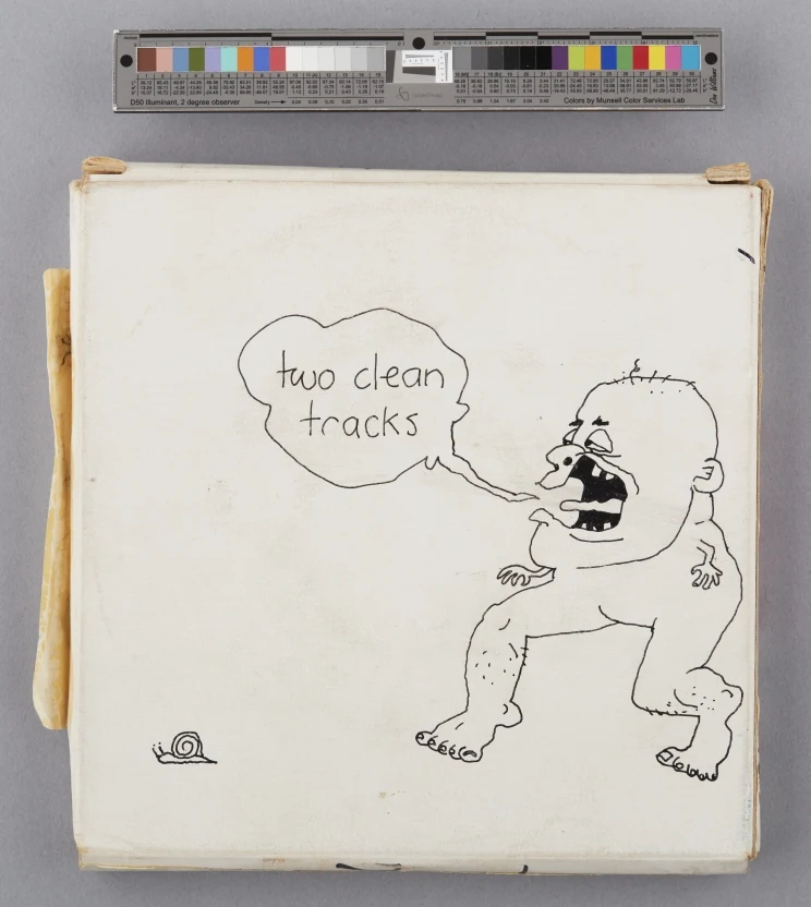 On the back of a cardboard magnetic tape reel box is a line drawing in black ink showing a character with stubby arms, human legs and feet and a large bald head chasing after a snail and saying the words, 'Two clean tracks' which appear in a speech bubble.