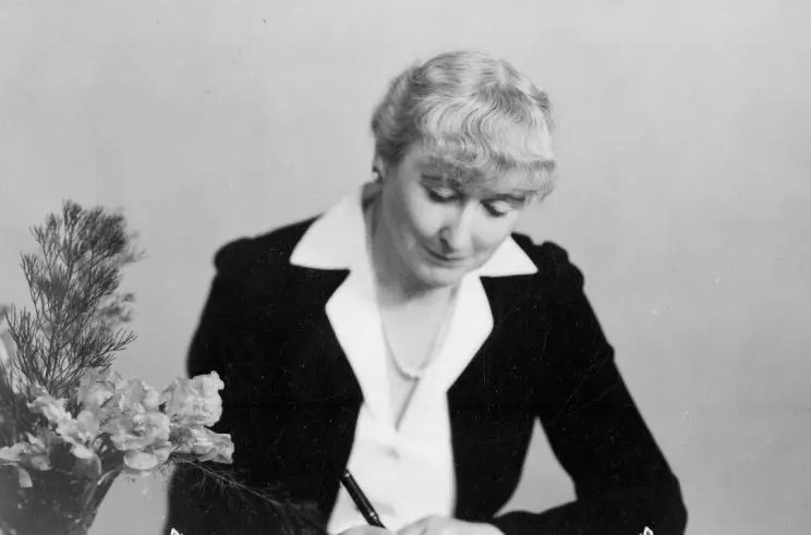 A woman seated at a desk, with pen in hand. 
