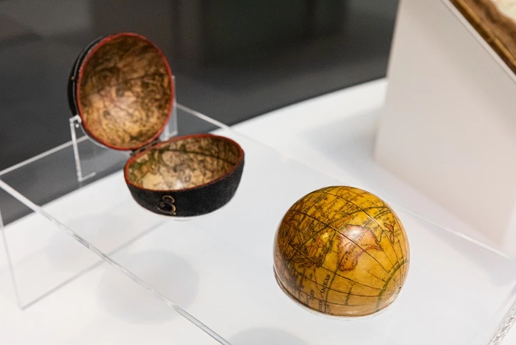 A faded miniature globe sits on a plastic display case along with its matching enclosure which is propped open like a clam shell.