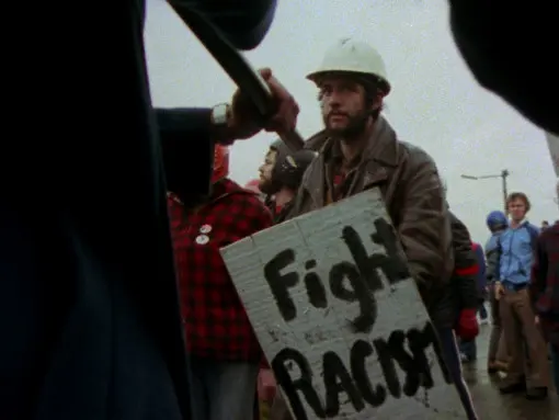 A man in a crowd carries a sign that reads Fight Racism.