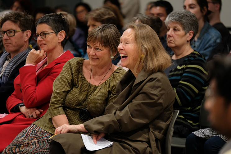 People in an audience reacting in different ways, some laughing some smiling, some looking solemn.