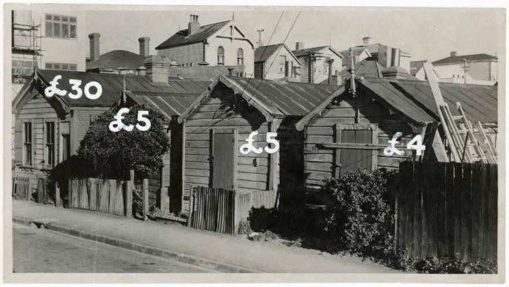 Four wooden houses closely situated together along a street with prices listed for each in pound sterling.