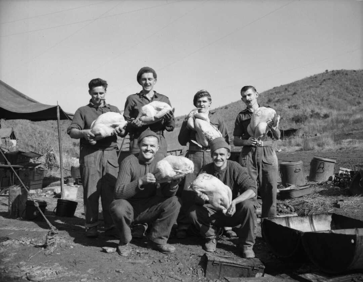 A group of six men posing for photo while holding raw turkeys ready for cooking.