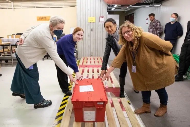 Four women touching a red box.