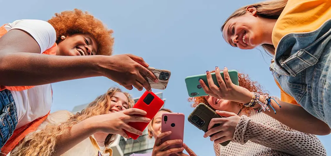 Low-angle view of a group of smiling teens looking at their smartphones.