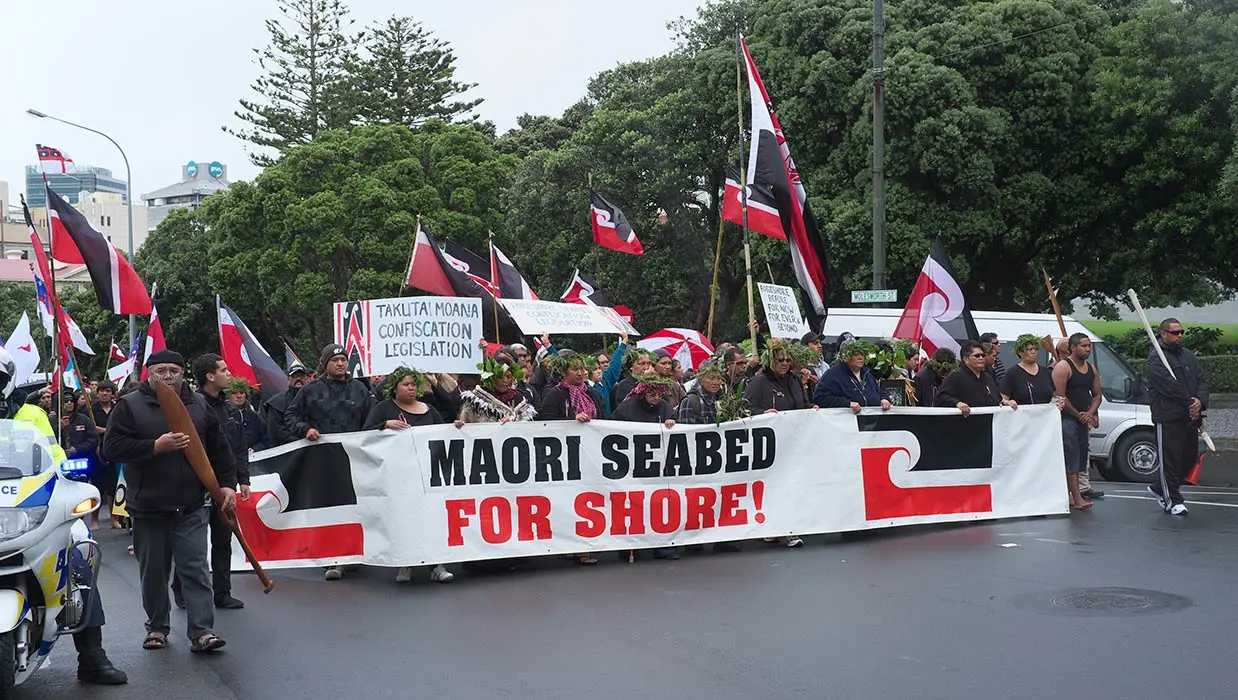Colour photograph of Foreshore and Seabed Bill protestors holding the Māori flag and a large banner 'Maori seabed for shore!'