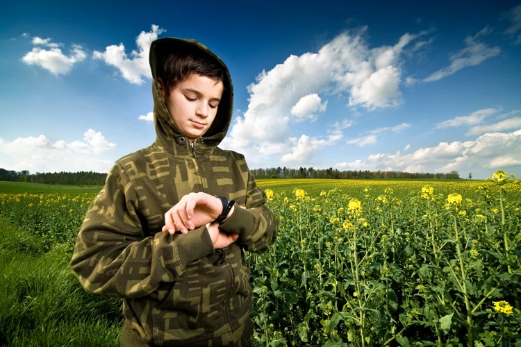 A boy checking his watch while standing in a field.