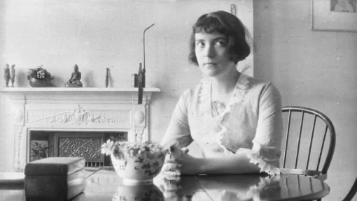 A black and white photo of a woman seated at a dining table. 