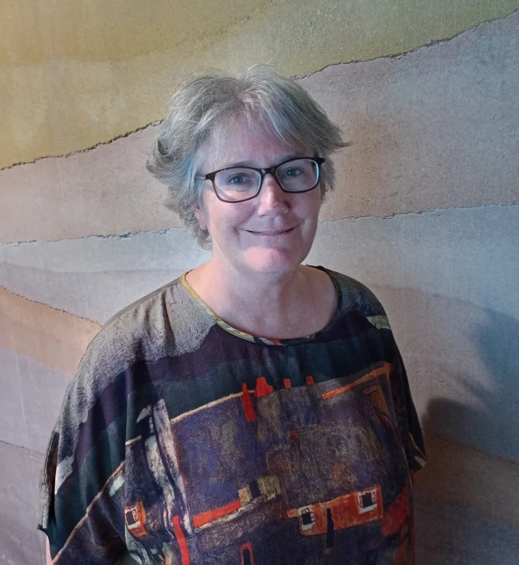 A portrait of a woman standing in front of a large artwork on the wall behind her.