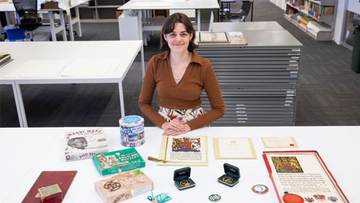 A woman standing behind a table on which sit an array of ephemera items. 