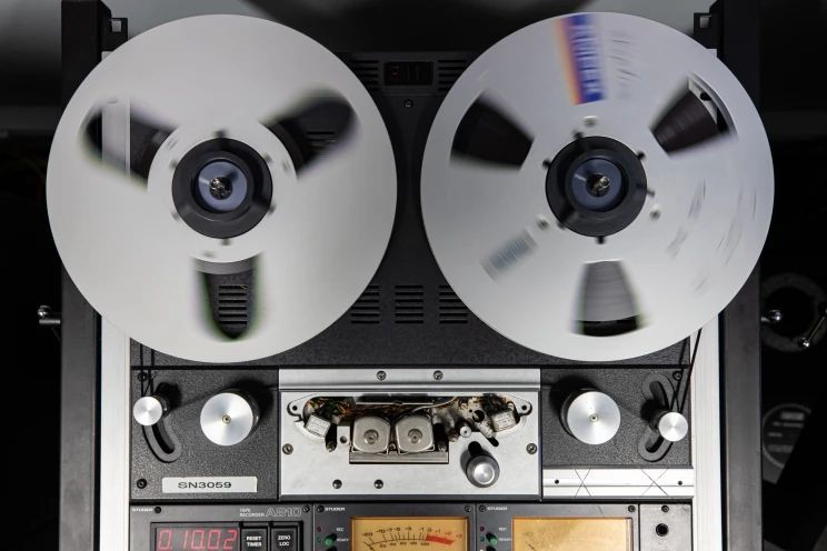 A large reel to reel tape machine with both spools appearing slightly blurry because they are in motion.