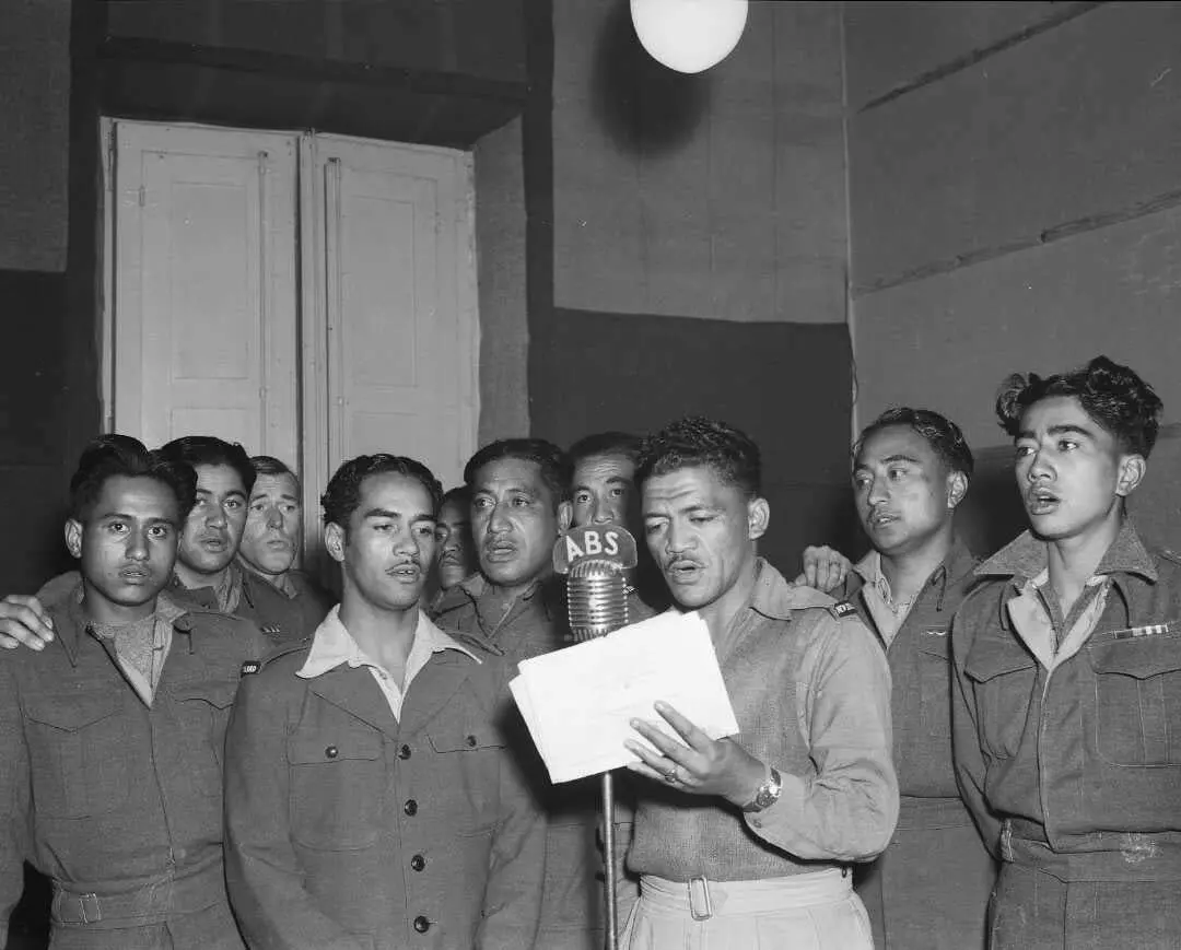 A group of Māori men standing around an old-fashioned microphone singing.