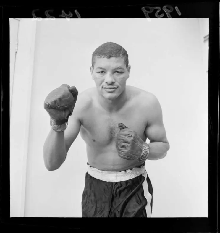 A black and white photo of a boxer wearing gloves and shorts. 