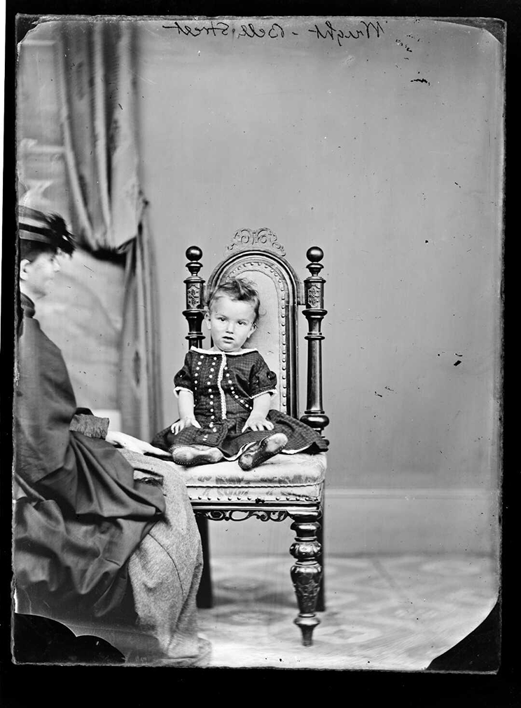 Black and white photo of a young child sitting in a chair, a woman is sitting close.