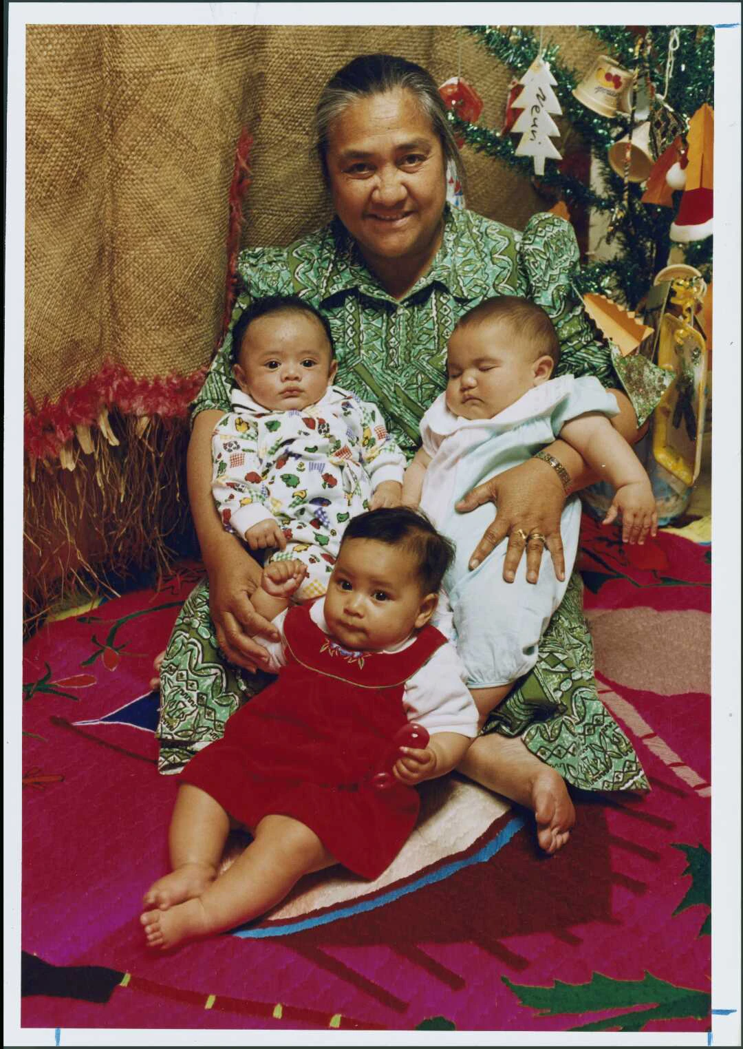Samoan woman setting on a colourful mat with three babies. 