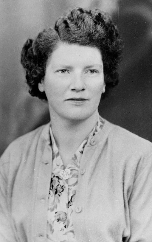 Studio portrait of a woman with short, wavy hair wearing a cardigan and floral blouse.