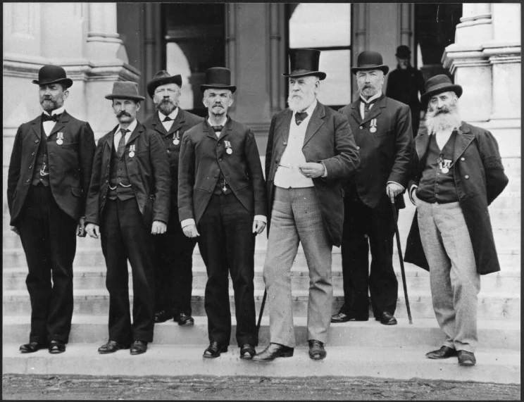 A black and white group portrait of male politicians standing on the steps of Parliament.