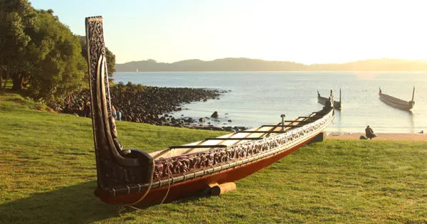 Carved Māori waka on beach with water and waka in background