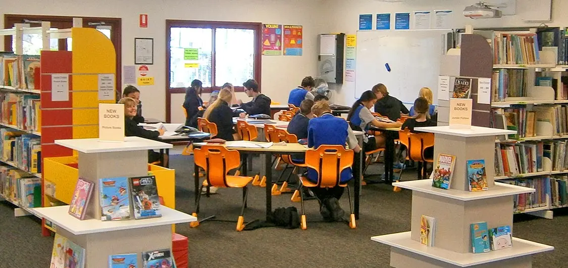 Group of students sitting at tables in a school library.