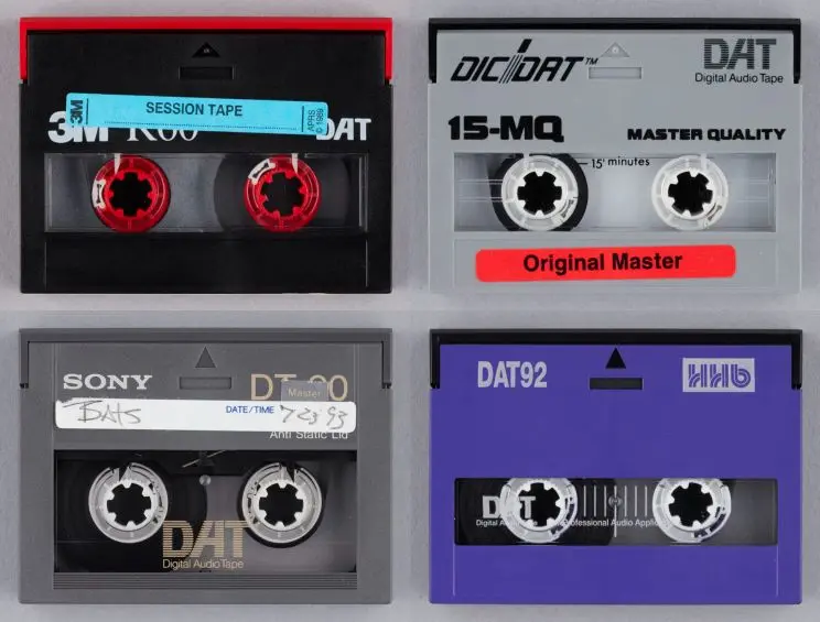Four different multi-coloured digital audio tapes that appear similar to cassettes with two spindles viewed through a window showing the tape that winds from one side to the other during playback. 