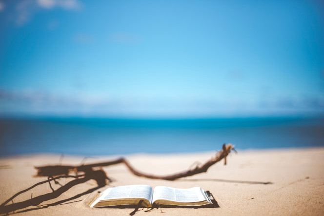 An open book on a sunny sandy beach.
