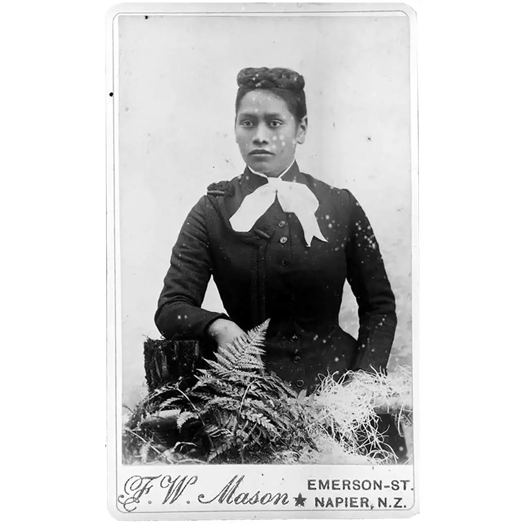 Copy of a cabinet card with a black and white studio photograph of Meri Te Tai Mangakāhia seated with plants. Below the photo are the words 'F W Mason Emerson Street Napier NZ'.