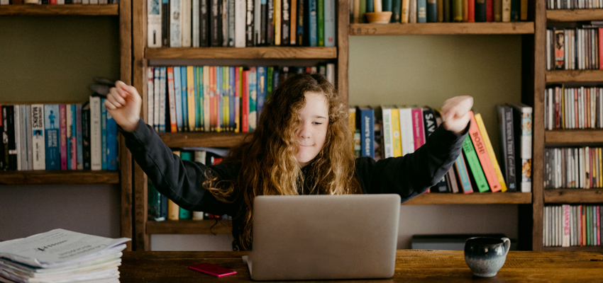 Student learning from home using a laptop and with a bookcase of books in background