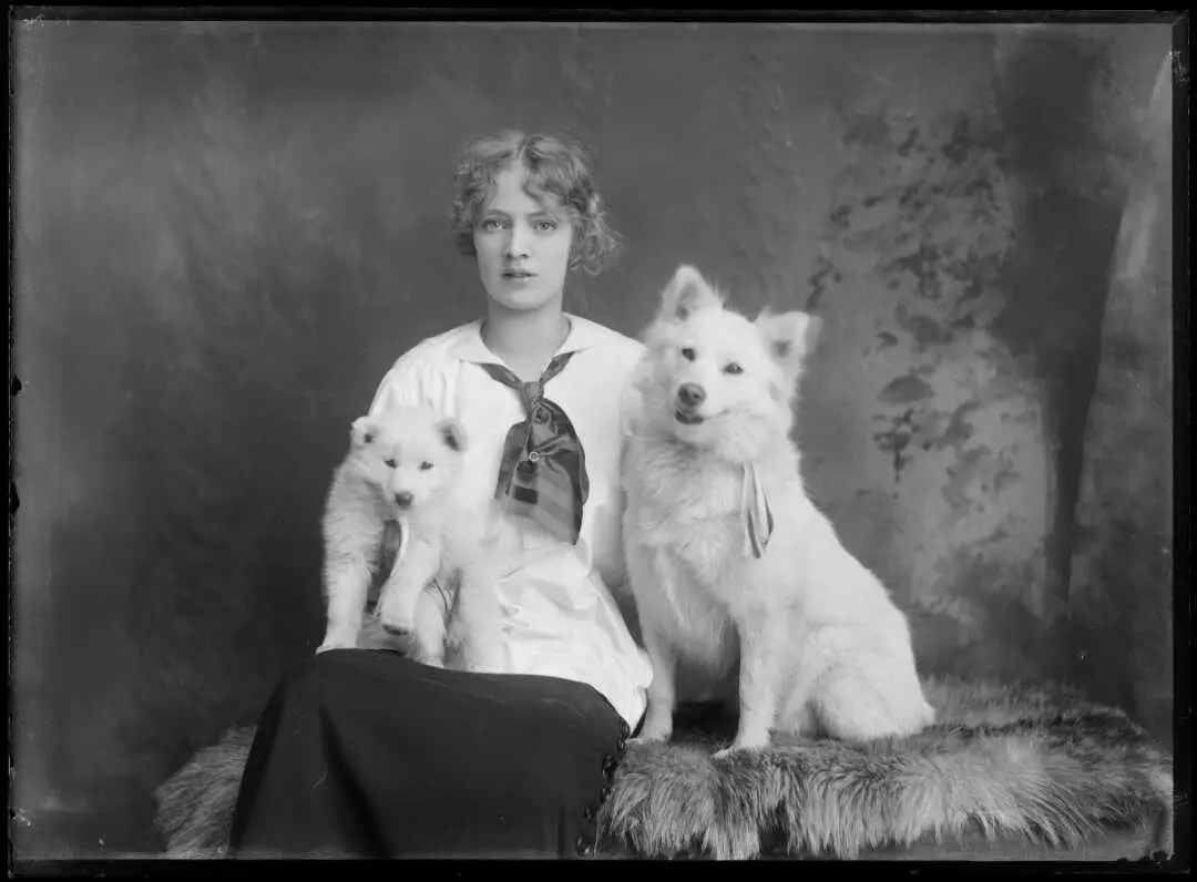 Black and white studio photo of a young woman with two fluffy white dogs. 