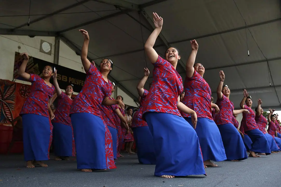 Colour photo of Pacific students performing a taualuga dance at ASB Polyfest. They are wearing a pēa or puletasi — a 2-piece dress with a patterned top and skirt.