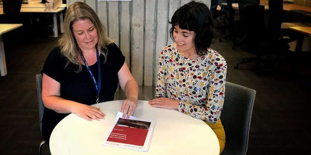 Services to School staff member looking at the School Library Development Framework document with a teacher seated at a table