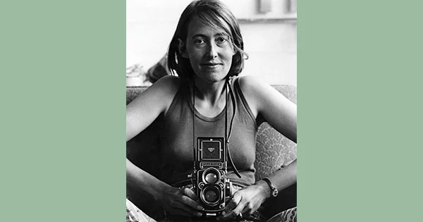 A women seated on a couch holding a waist-level twin-lens camera.
