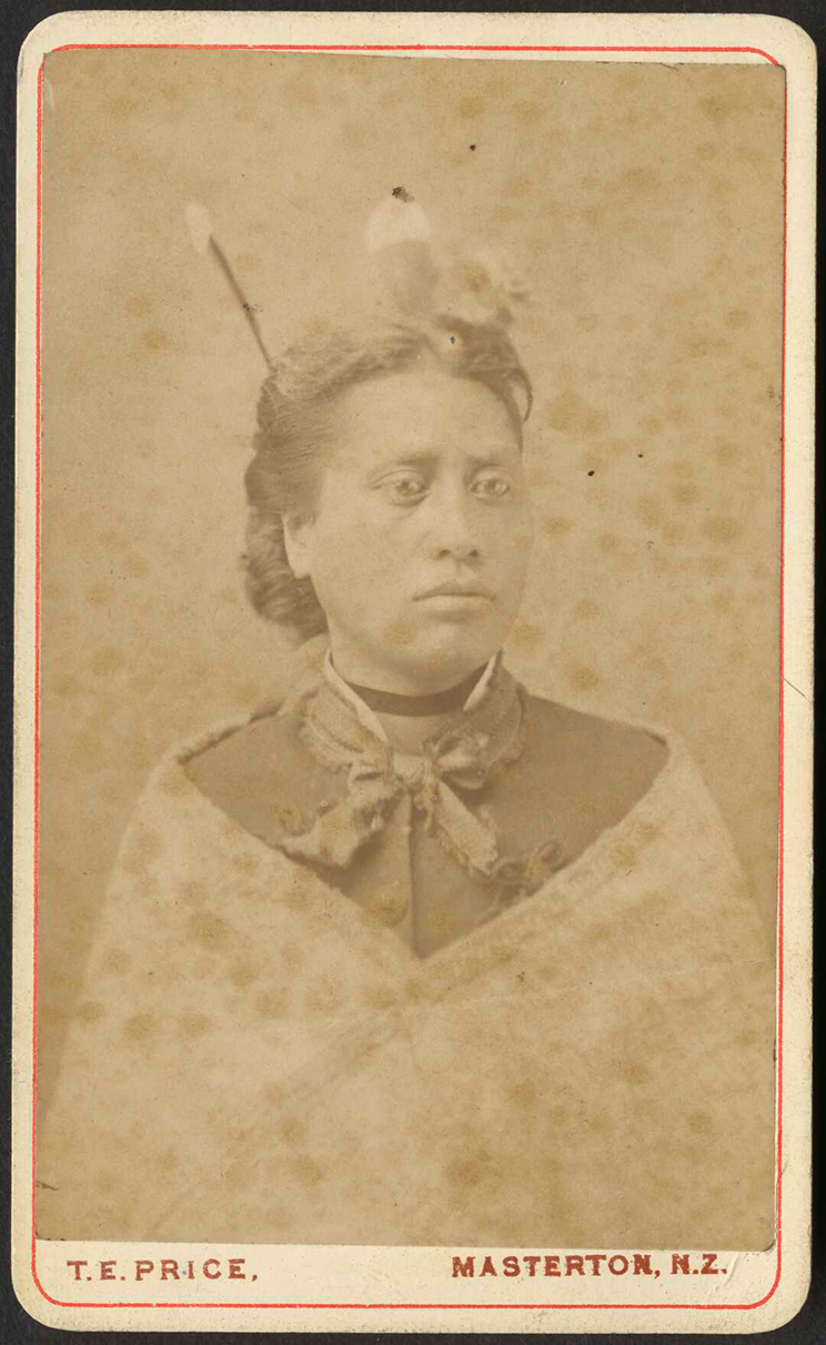 Portrait of a Māori woman wearing Victorian clothes. She has hui feathers in her hair. 