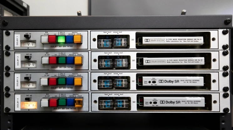 A rack of four similar electronic controllers with five buttons of differing colours and what appear to be white tapes with the words, 'Dolby SR' on them.