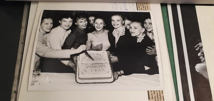 A group of smiling women hold a cake up to the camera so the writing on it is visible.