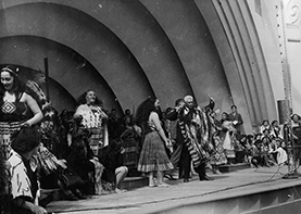 Māori kapa haka group performing on a stage with a shell like background. 