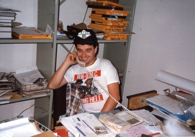 Shows Cammick seated at a desk and speaking on the phone. After a one year hiatus, Murray Cammick resumes the Rip It Up editorship in 1988. Photo: Chris Bourke.