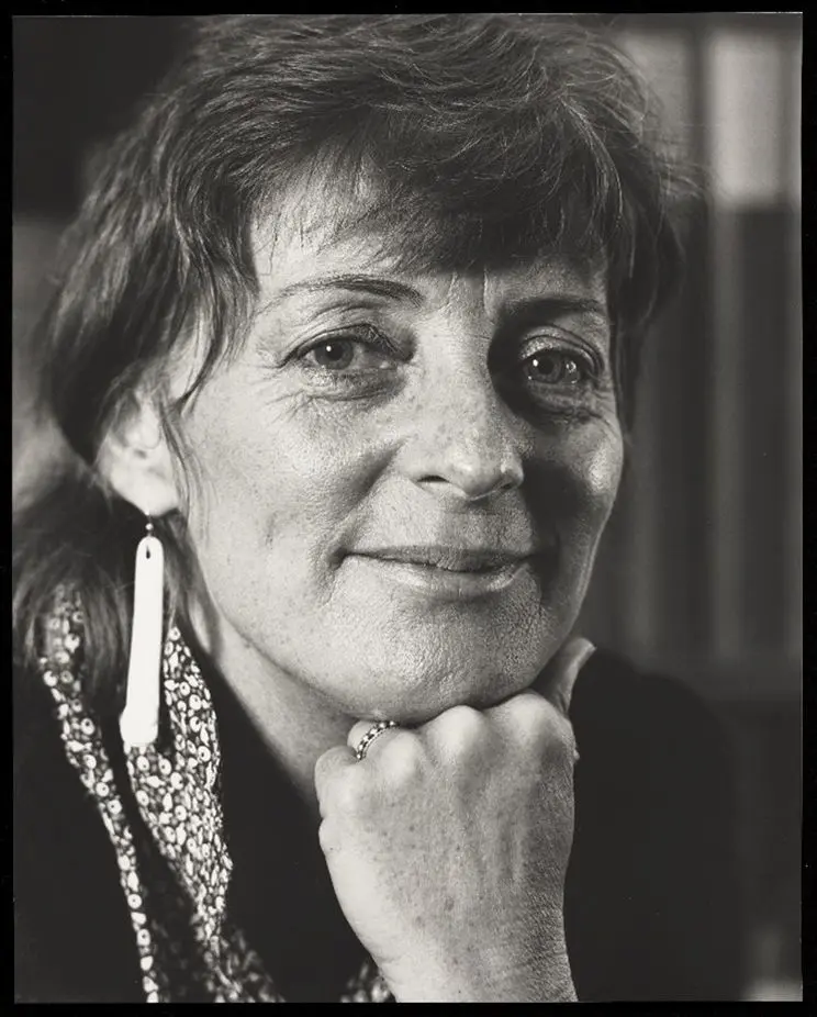 A black and white portrait of a woman, smiling, with her head resting on her knuckles. 