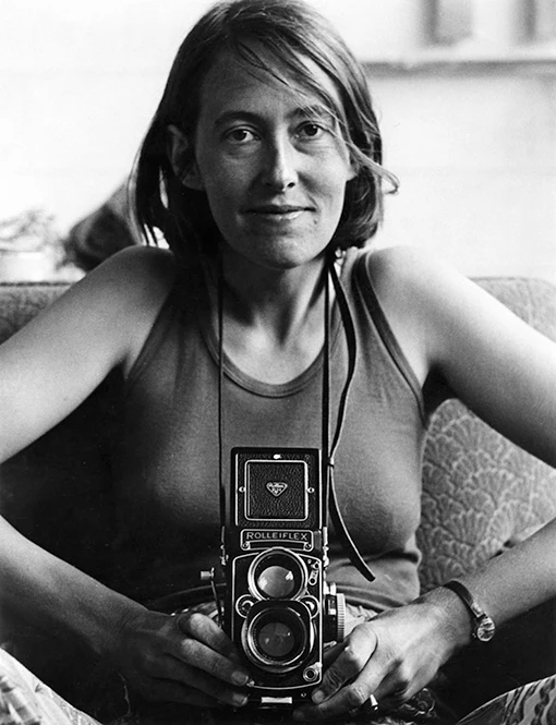 A women seated on a couch holding a waist-level twin-lens camera.