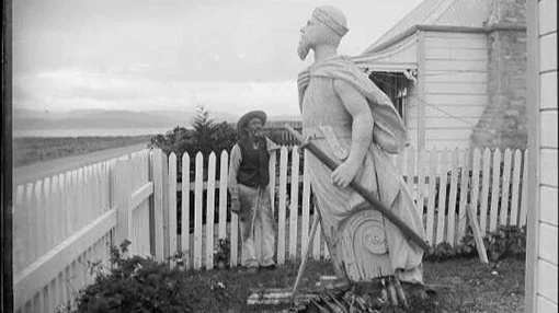 Photo of a man looking at a large statue of a Viking-style man leaning forward into the wind.