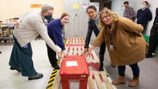 Four women touching a red box.
