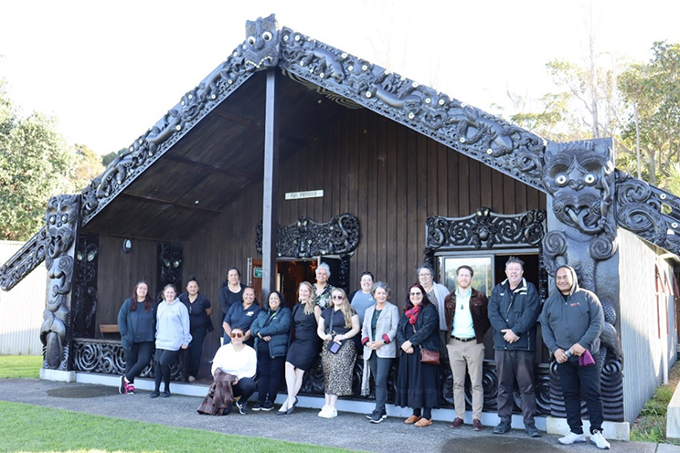 A group standing in front of a marae wit beautiful carvings. 
