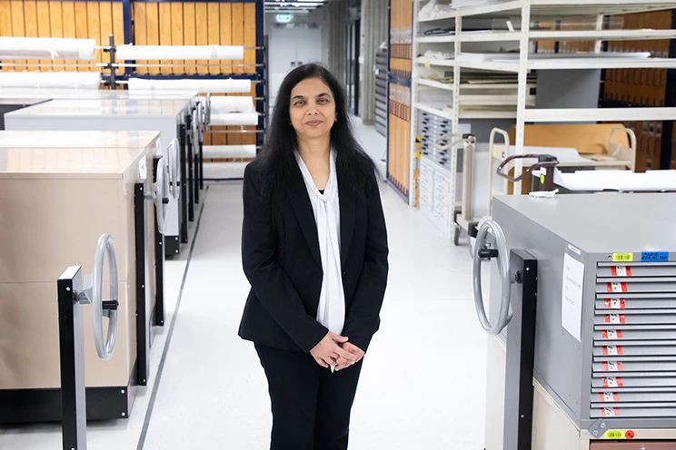 A woman wearing a black jacket and a white blouse in a room full of grey metal storage cabinets.