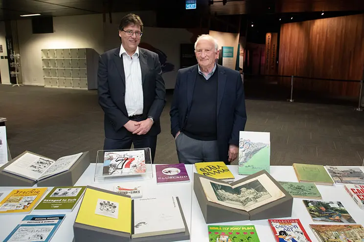 Two men looking at a display of books open on a table. 