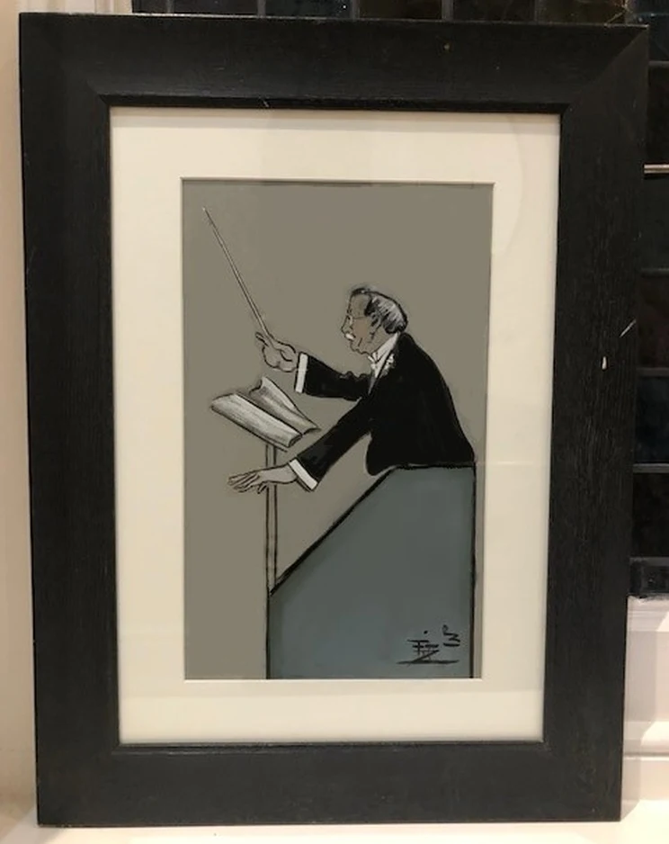 A small, framed caricature showing a conductor with black waistcoat and baton standing behind a podium holding a book of music.